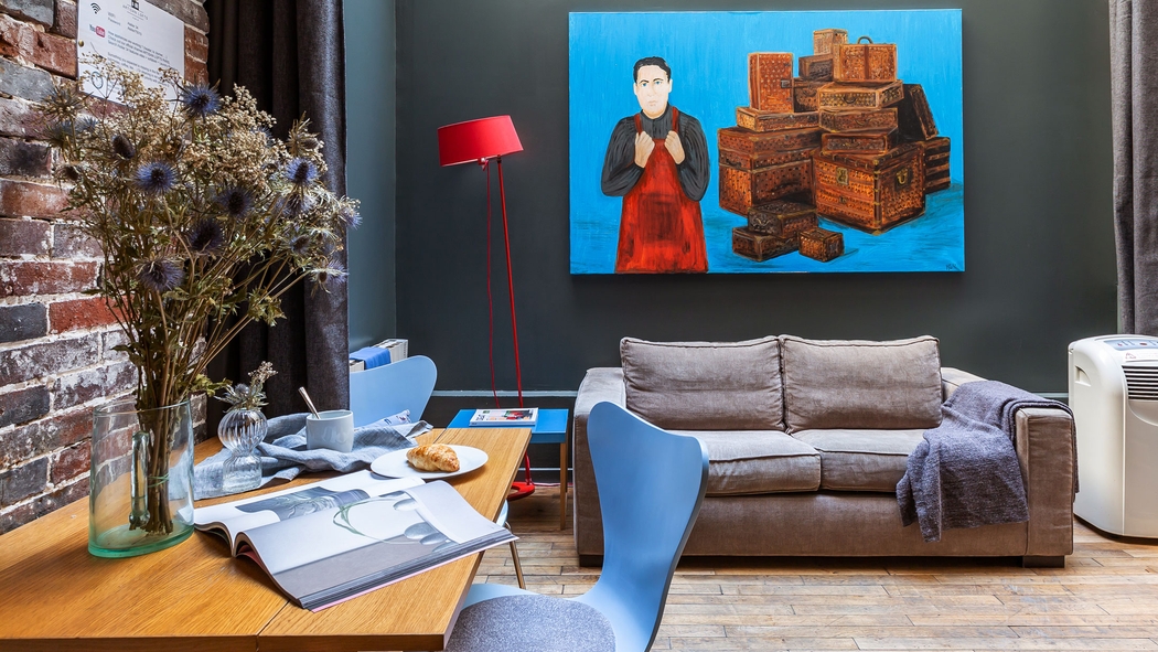 A chic space features a desk, a comfy sofa and a large piece of art.
