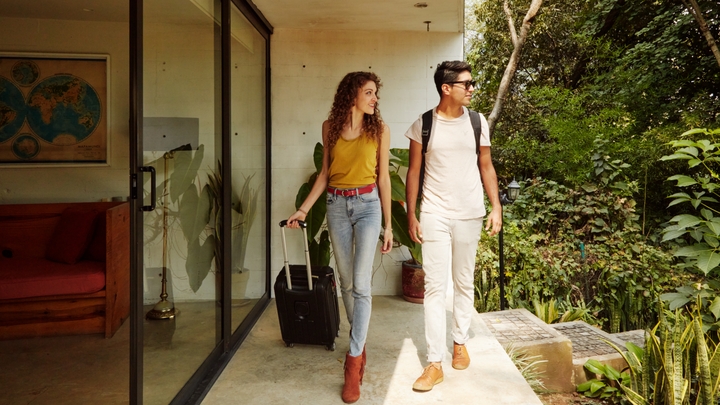 Two guests, with backpacks and a roller bag, arrive at home with a sliding-glass door entryway.