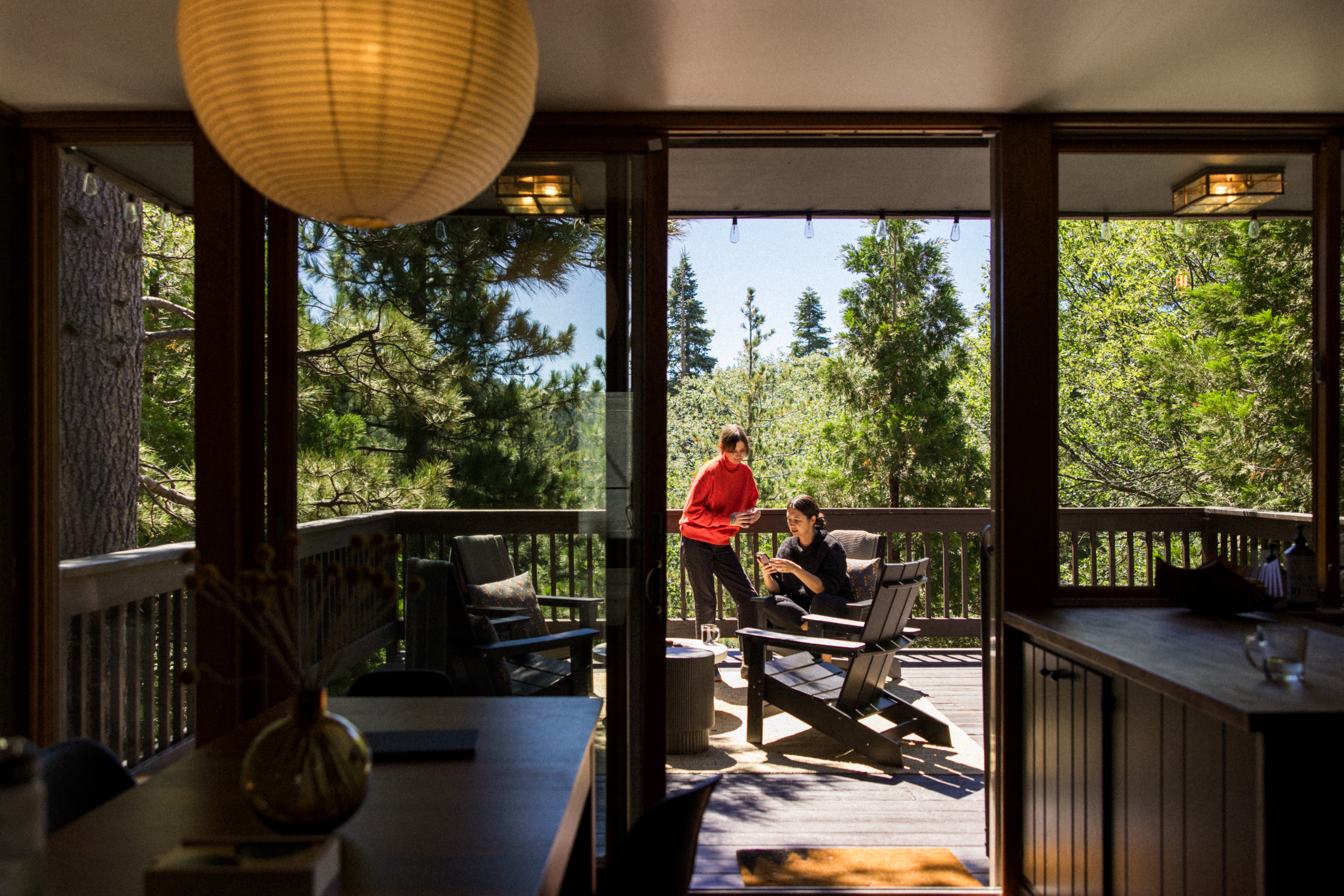 Manneskja í símanum, umkringd furutrjám, situr í Adirondack-stól. Önnur manneskja er standandi með bolla í hönd.
