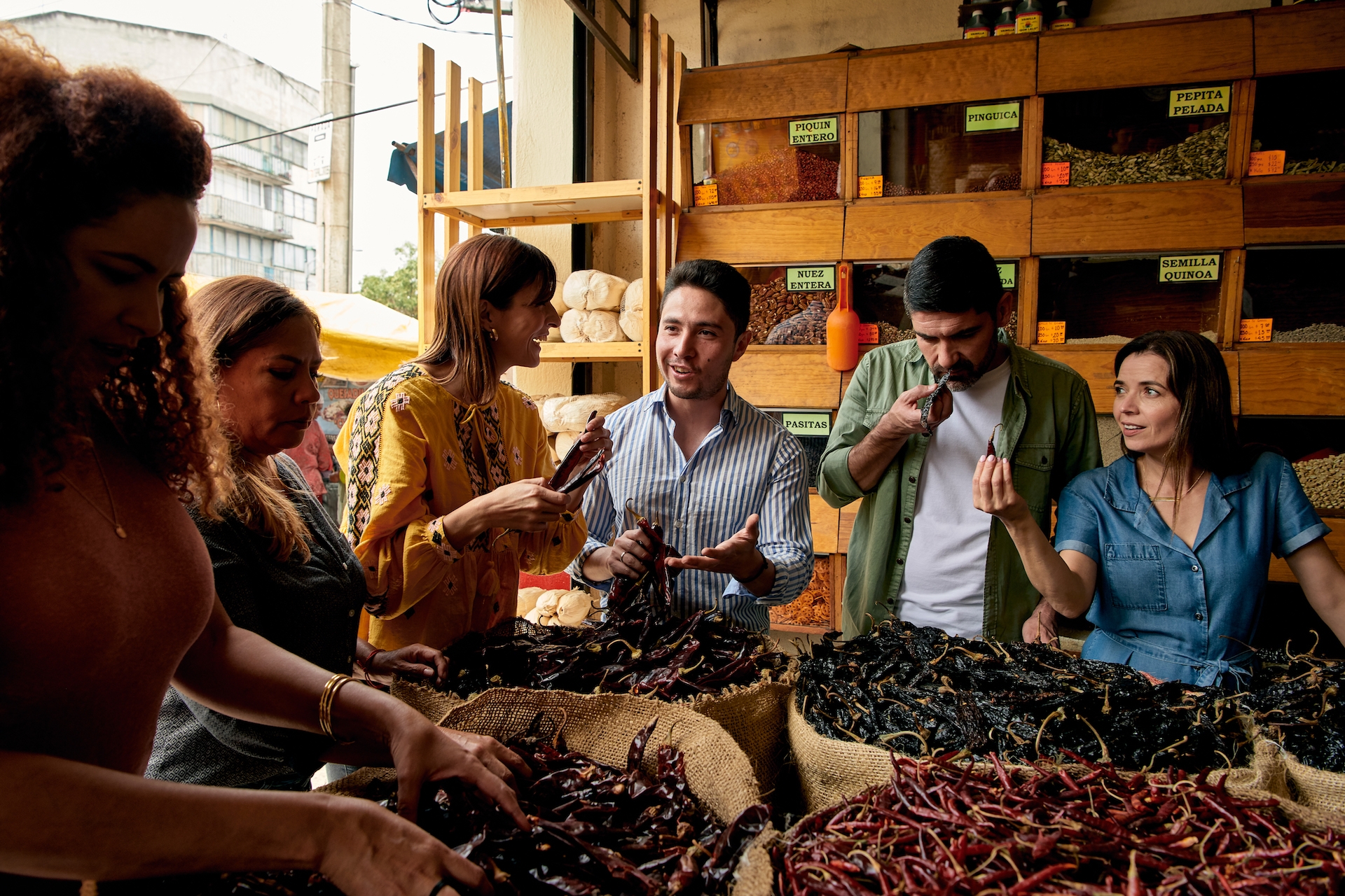 Организатор Впечатления в торговом лотке на рынке Мехико рассказывает гостям о видах сушеного перца чили.