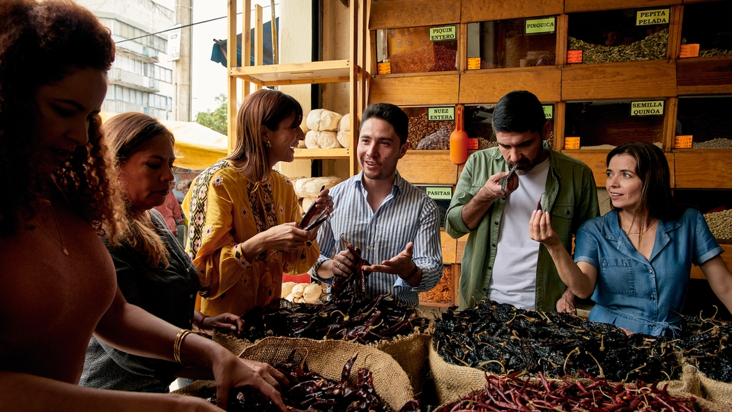 In een marktkraam in Mexico-Stad vertelt een host van een ervaring de gasten over verschillende soorten gedroogde chilipepers.