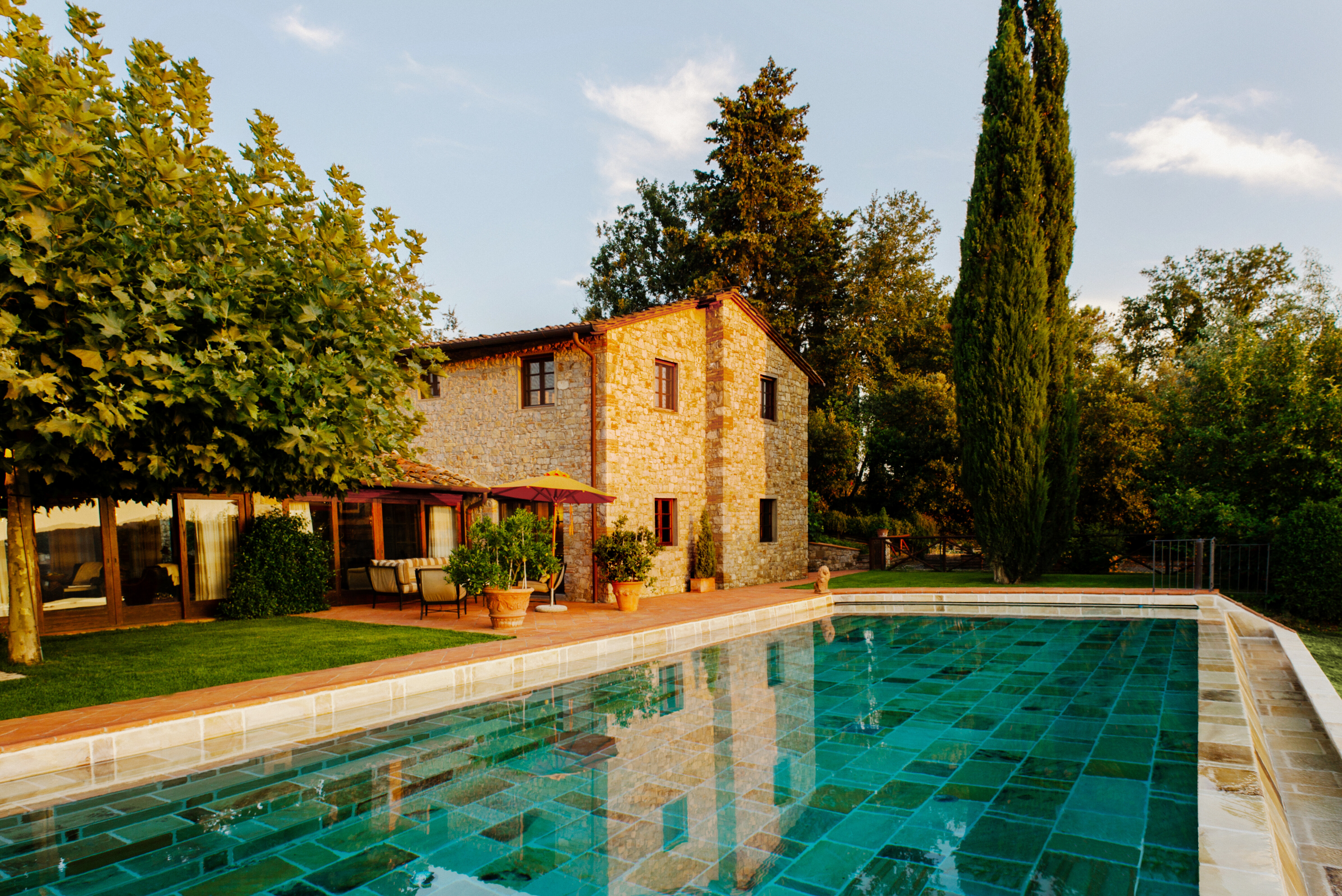 Der Garten einer Unterkunft mit einem Swimmingpool im Vordergrund und dem Haus, einer Terrasse und Bäumen im Hintergrund.