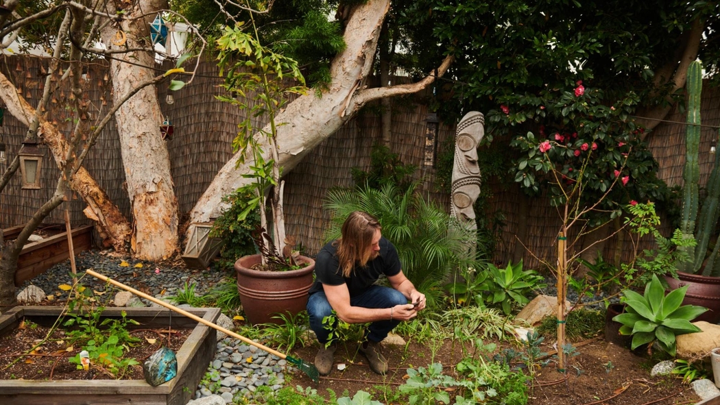 Ein Mann in Jeans und einem marineblauen Shirt arbeitet an einem Garten im Hinterhof.