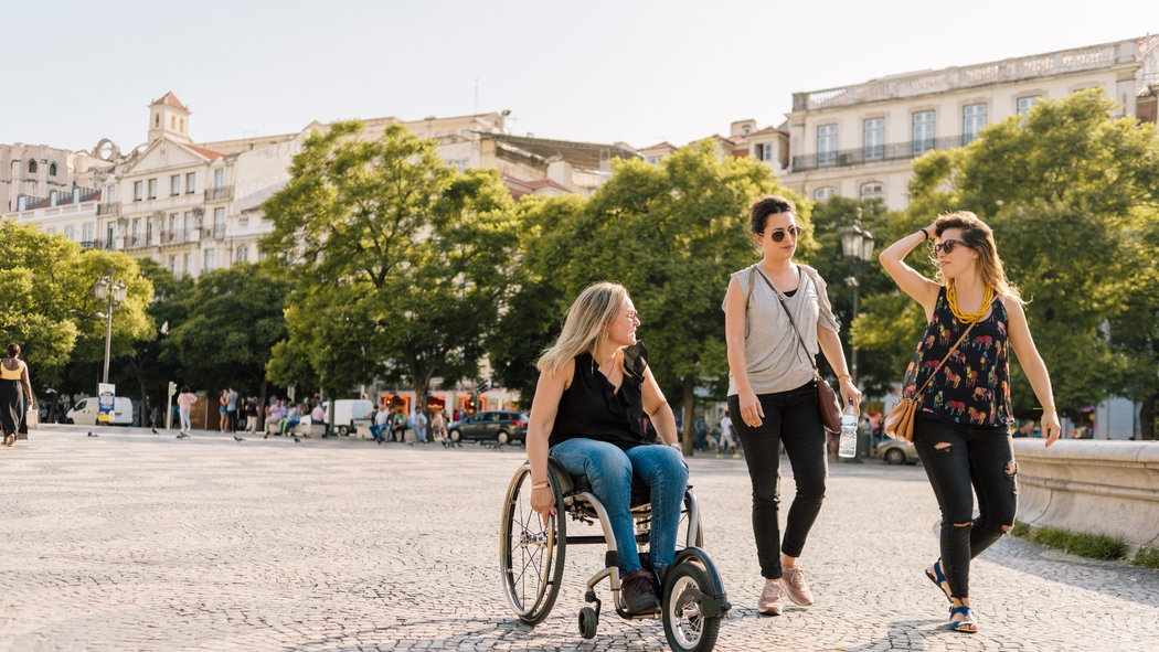 Host and two guests on a tree-lined cobblestone street; one guest is using a wheelchair