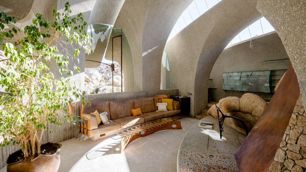 La sala semienterrada de Kellogg Doolittle House tiene una gran chimenea de piedra y un sofá de piel envejecido integrado en el espacio.