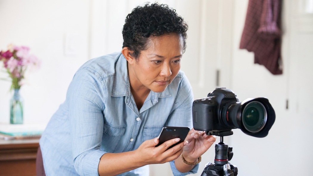 Um anfitrião com cabelo curto usando uma camisa azul tirando uma foto com uma câmera DSLR