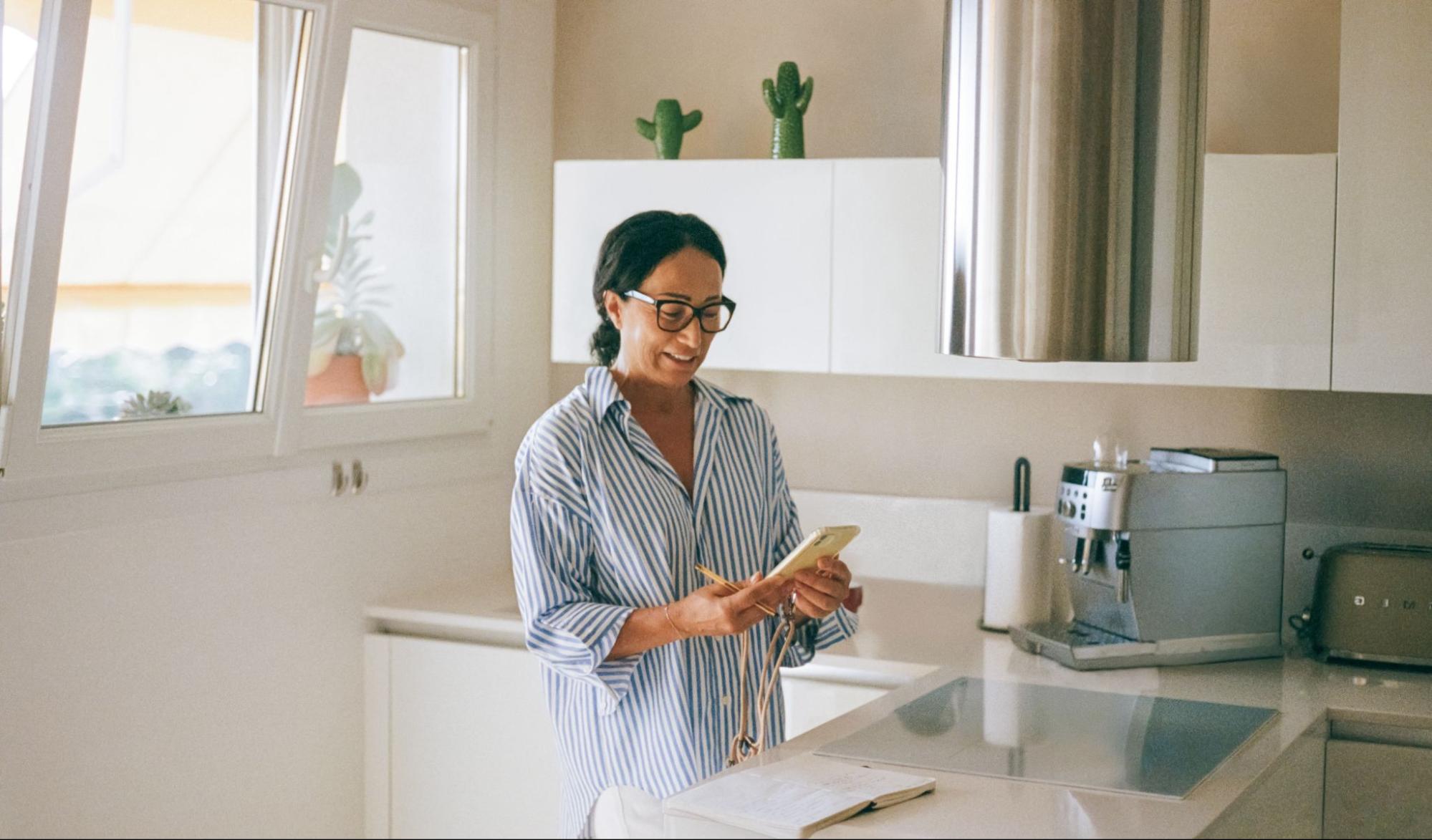 Una persona está de pie mirando su teléfono en una cocina con muebles blancos.