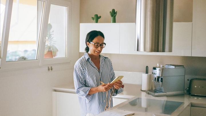 Une personne se tient debout et regarde son téléphone dans une cuisine dotée de placards blancs.