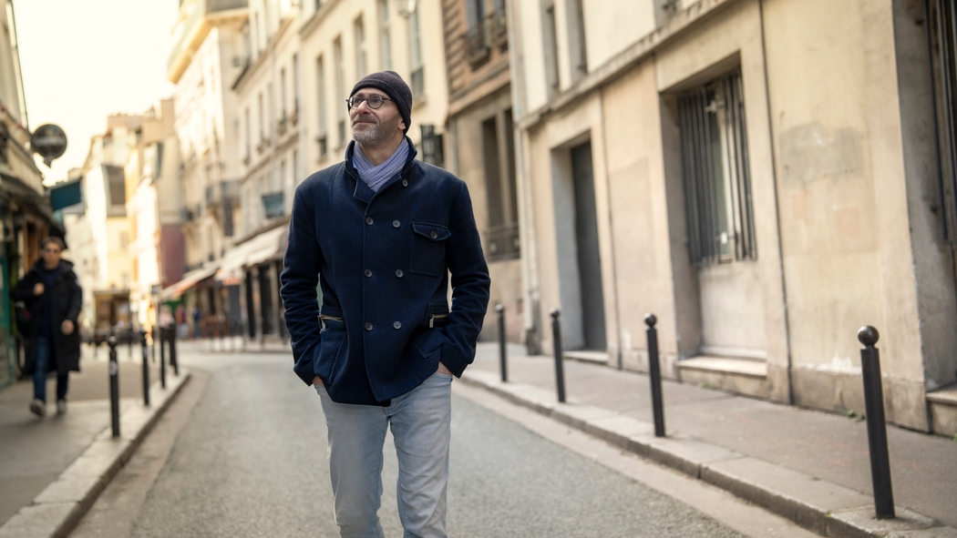 一位戴眼鏡、身穿藍色外套的人步行經過巴黎的一條石春路。