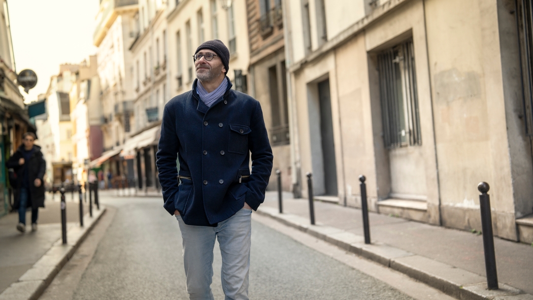 En person med glasögon och en blå jacka går längs en kullerstensgata i Paris.