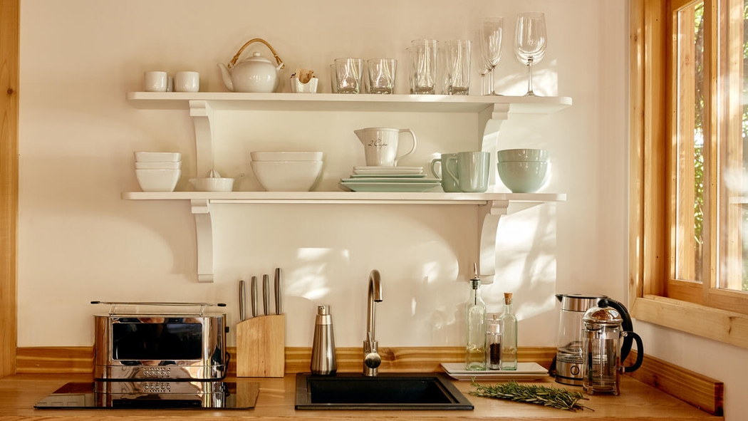 A kitchen counter and sink with white shelves of dishes and pots above it.