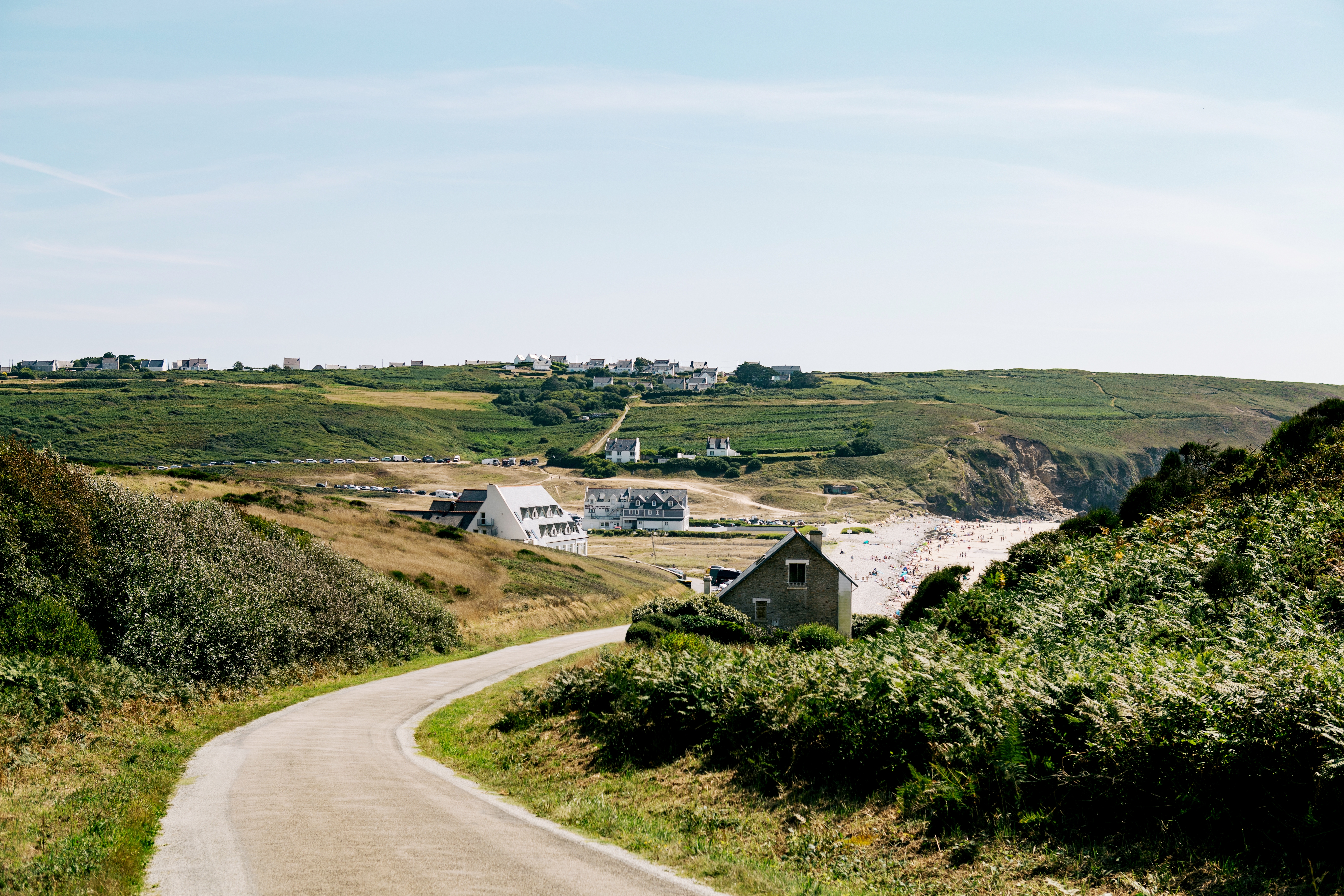 Hi ha un camí rural buit que passa per unes cases disperses i una platja.