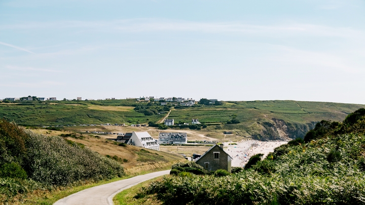 A quiet country lane winds past a few scattered houses and a beachfront.