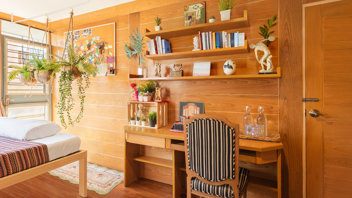 Sunlight floods a bedroom with a narrow desk and shelves built into wood paneling. A dozen plants help create a natural vibe.