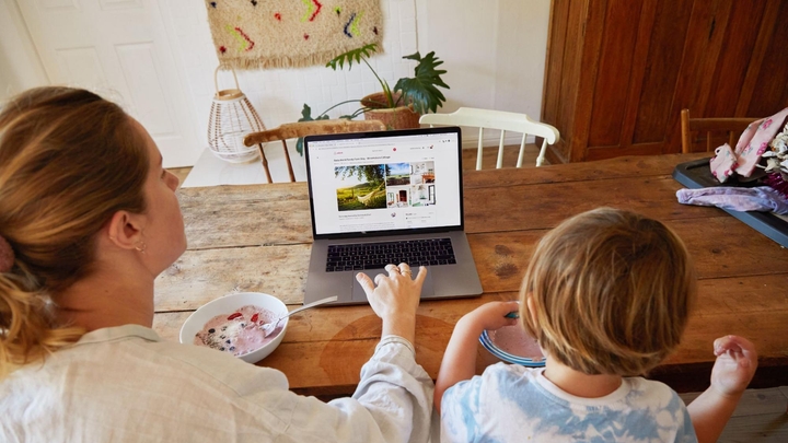 Umntu omdala ubuka into enokubhukishwa ka-Airbnb kwi-laptop ngoxa ehleli kwitafile eyenziwe ngeplanga kunye nomntwana omncinci. Bobabini batya iyogathi neziqhamo.