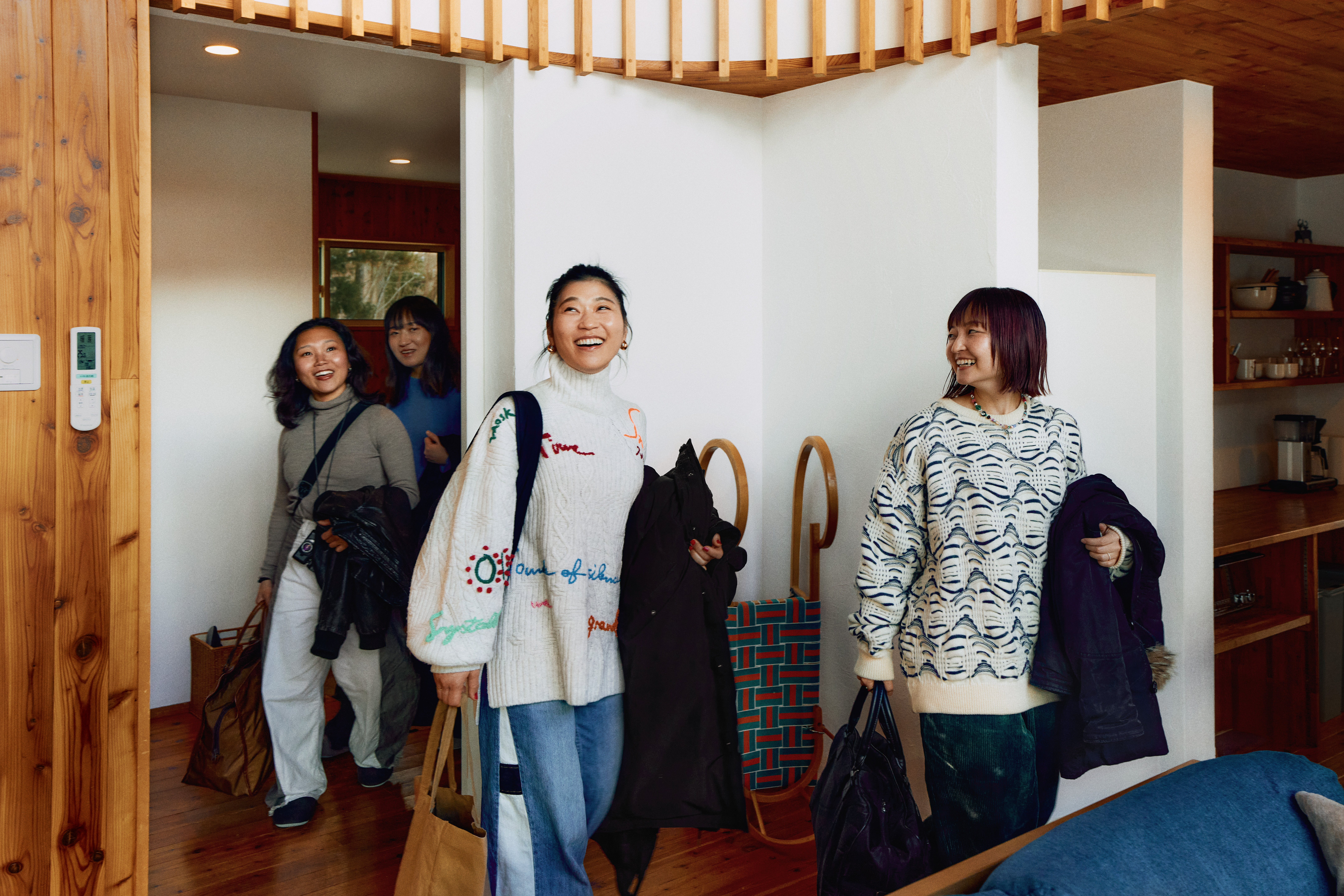 Cuatro personas sonrientes que llevan en la mano chaquetas, bolsas de tela y más equipaje entran en un alojamiento.