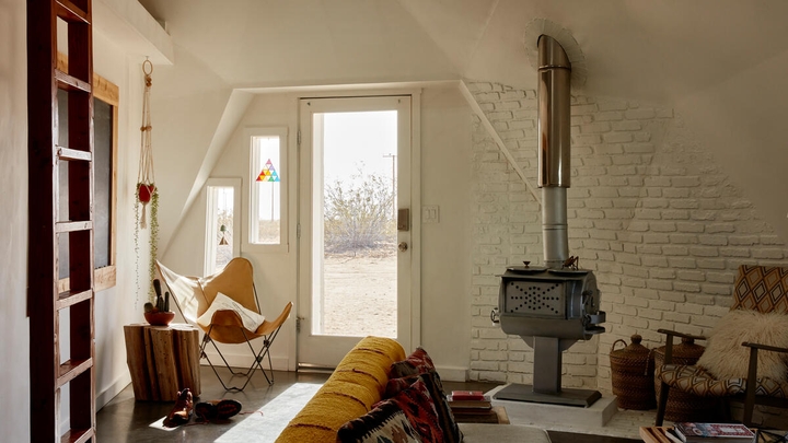 A rustic, light-filled living room with a wood-burning stove and yellow couch.