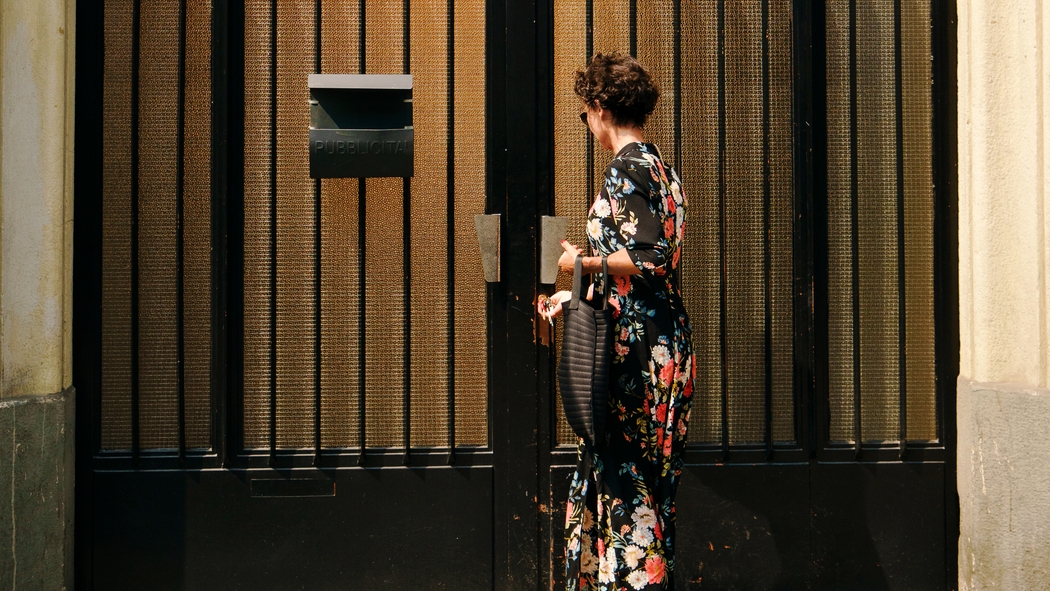 A woman in a floral dress unlocks the front door to a building.