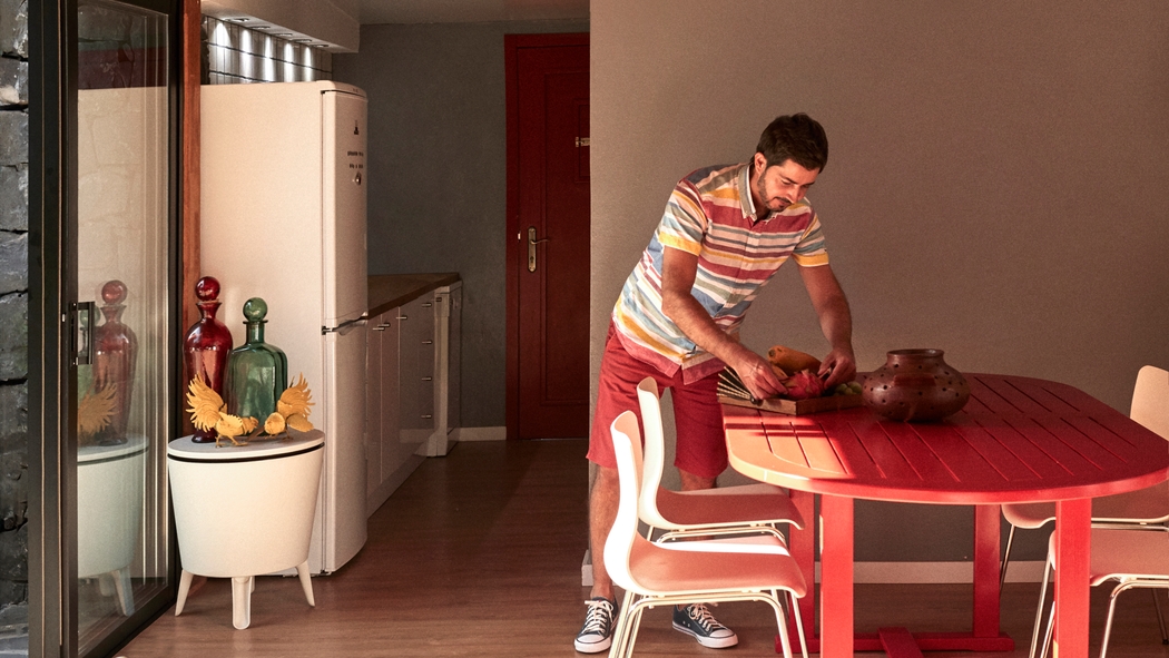A person in a striped shirt organises items on a red dining table that overlooks sliding glass doors.