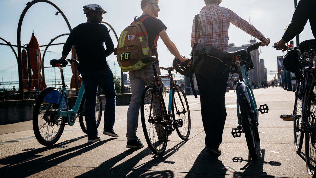 Un groupe d'hôtes Airbnb marche avec des vélos lors d'une journée ensoleillée en ville.