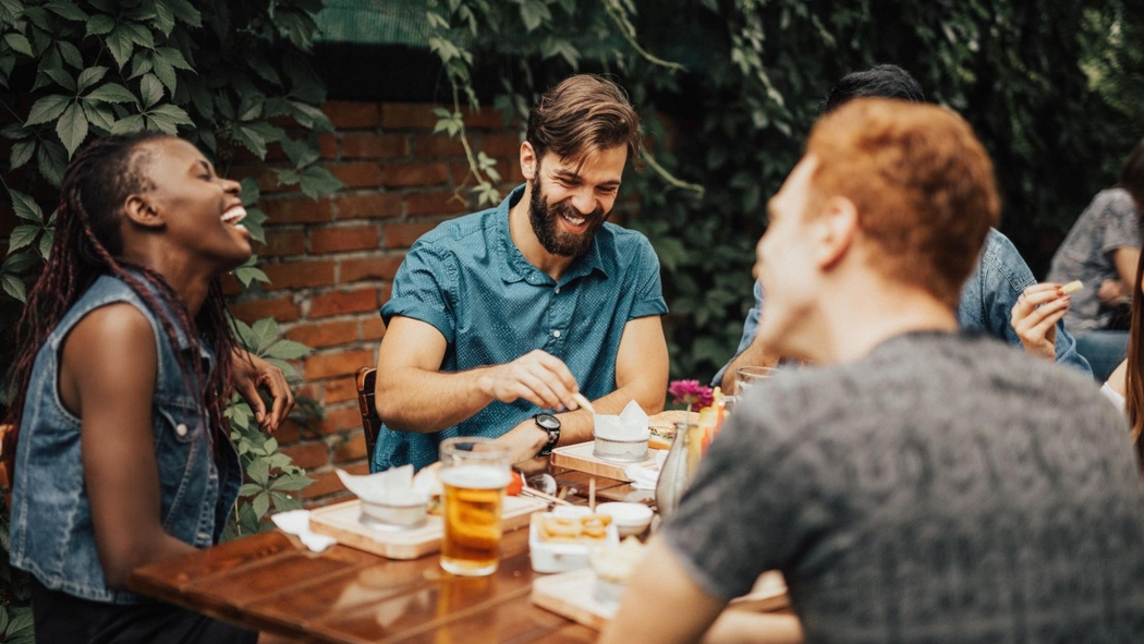Eine befreundete Gruppe sitzt lachend draußen an einem Tisch und isst.