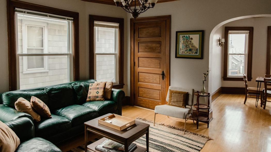 Image alt text: A tidy living space features shining hardwood floors, a green couch, and large windows overlooking neighboring houses.