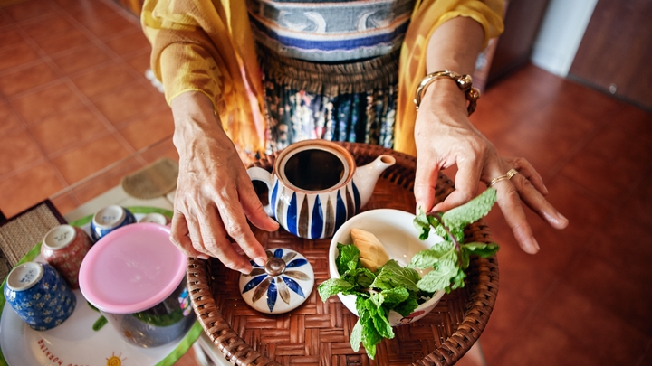 Uma pessoa prepara um tabuleiro de chá com um bule e hortelã fresca.