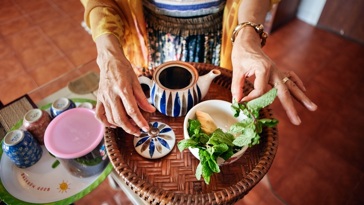 A person arranges a tea tray with a teapot and fresh mint.