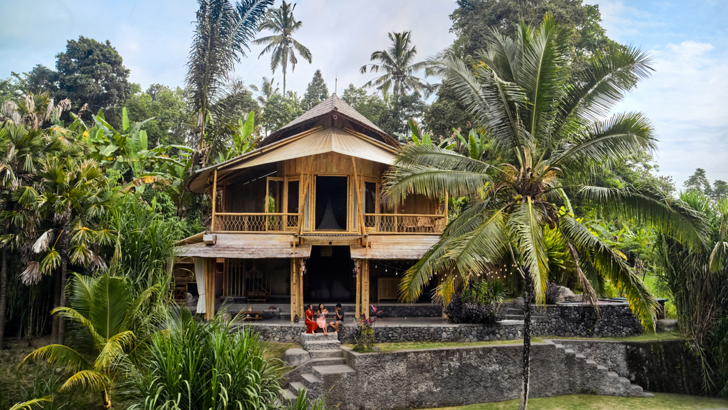 Tre persone siedono sui gradini di un alloggio Airbnb a Bali di fronte a grandi alberi tropicali e alla vegetazione.