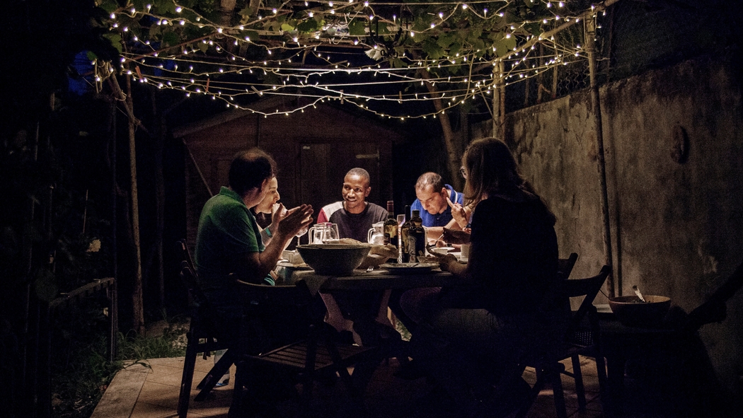 Un groupe de personnes assises autour d'une table en extérieur discutent et mangent ensemble.