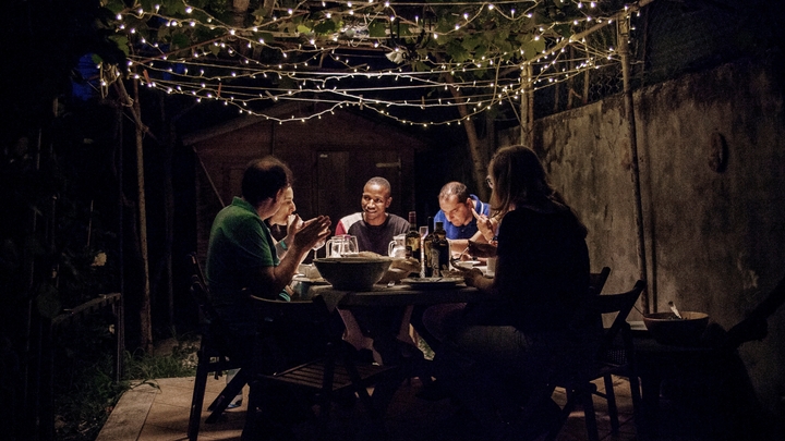 A group of people sits at a table outside, talking and eating.