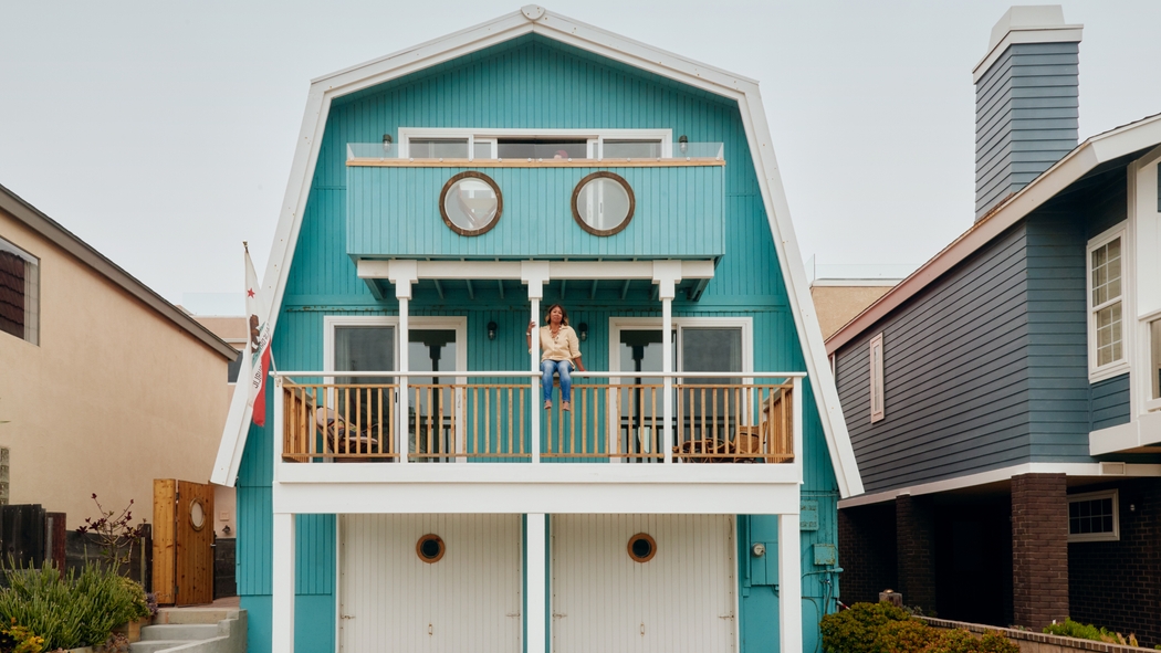 Een vrouw zit op het balkon van een blauw huis.
