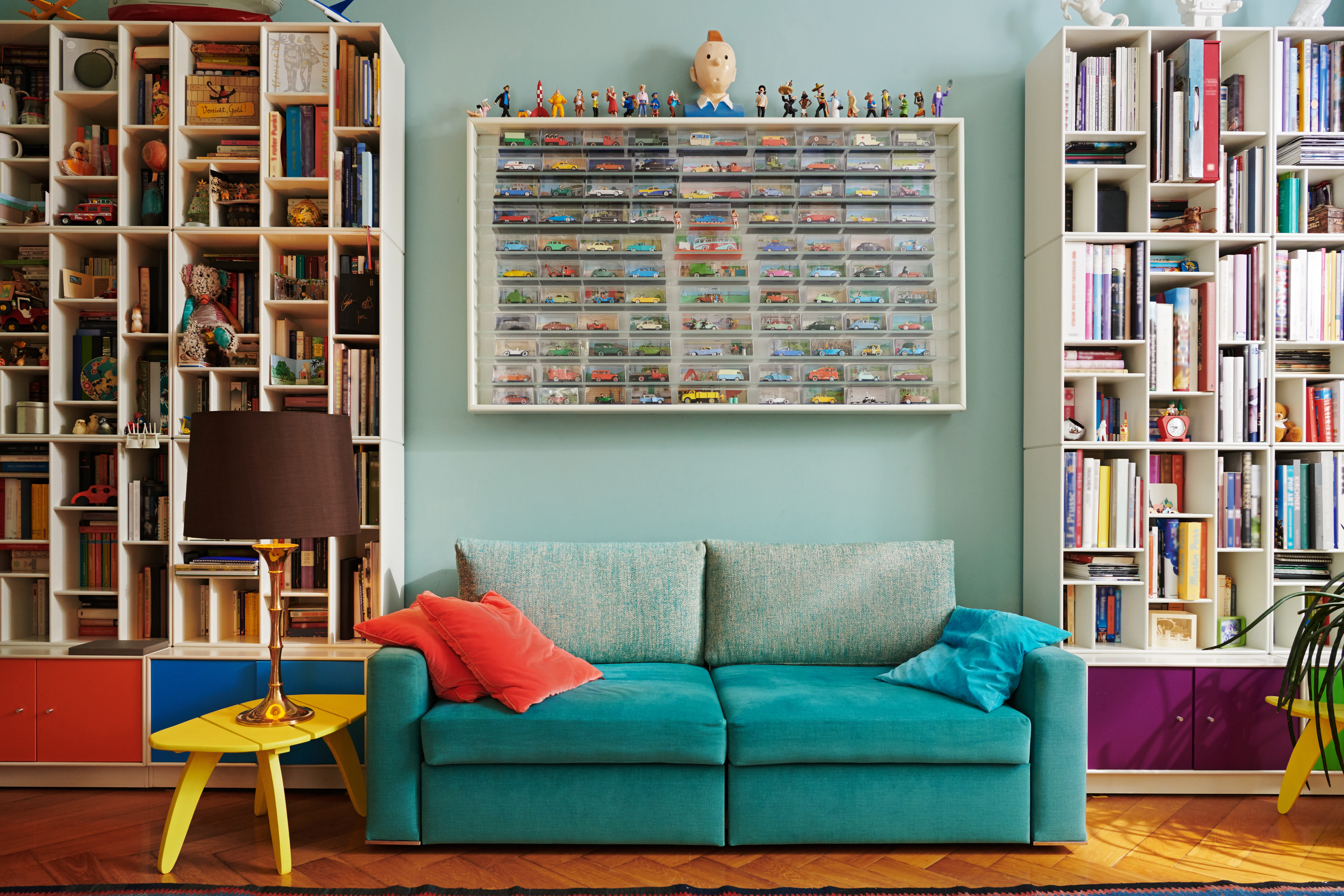 Libros, autos de juguete y varios adornos cubren las repisas de una pared detrás de un sillón verde azulado.