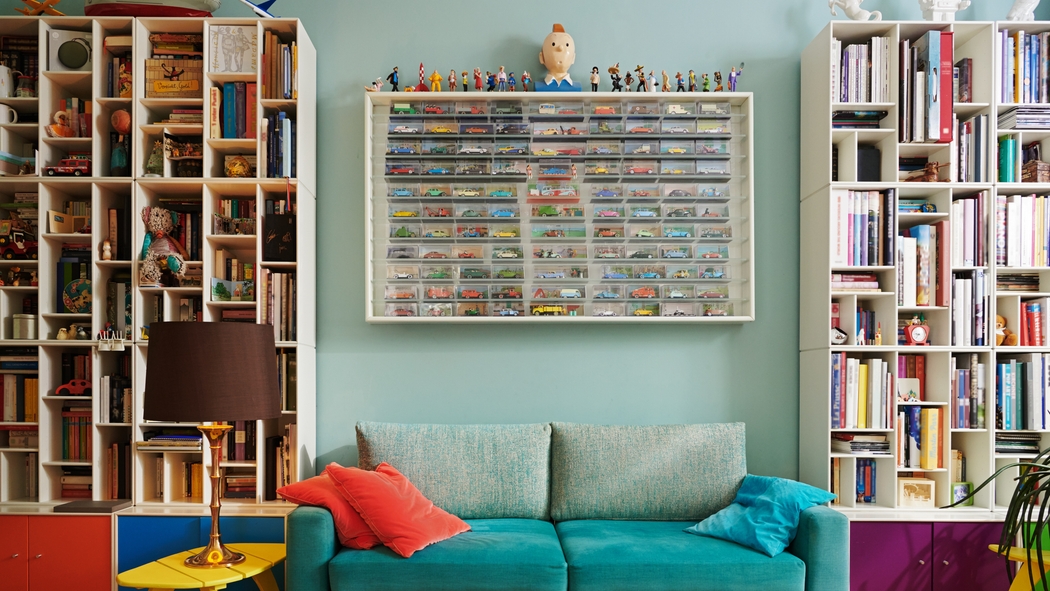 Books, toy cars and knick knacks line a wall of shelves above a teal couch.