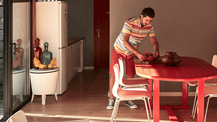 Persona, tērpusies svītrainā pogājamā kreklā, sakārto sarkanu ēdamgaldu pie bīdāmām stikla durvīm.