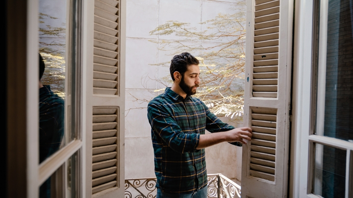 Osoba u kariranoj košulji i farmerkama pregledava kapke na francuskim vratima koja se otvaraju na balkon.