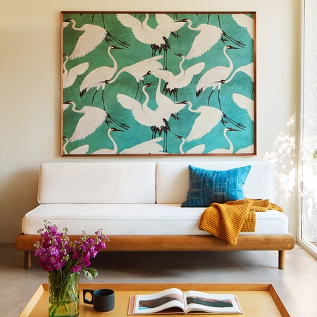 Một bức tranh sơn dầu vẽ đàn chim diệc được treo trong căn phòng đầy nắng có kệ sách kê sát một mặt tường; phía trước là một chiếc bàn trà.
