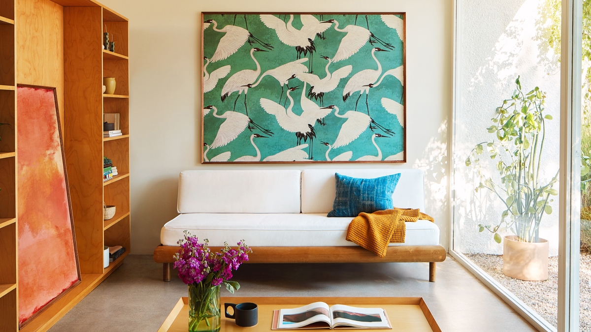 A painting of herons anchors a sunny room with bookshelves along one wall and a coffee table in the foreground.