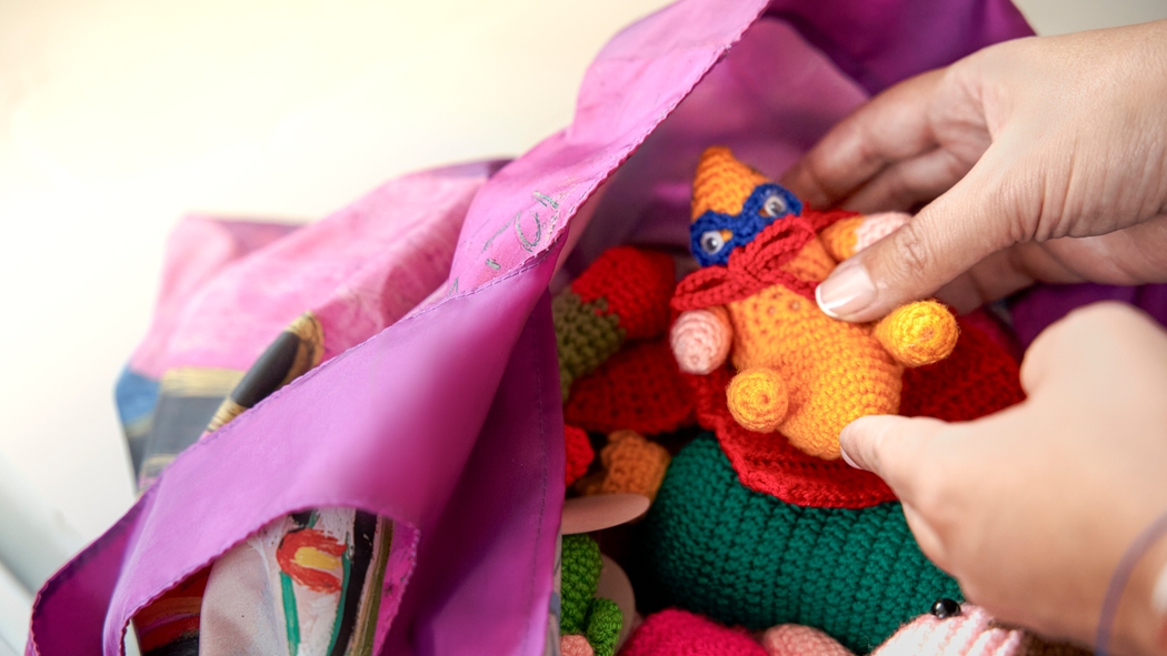 A person holds up a handmade doll inside a bag of several dolls.