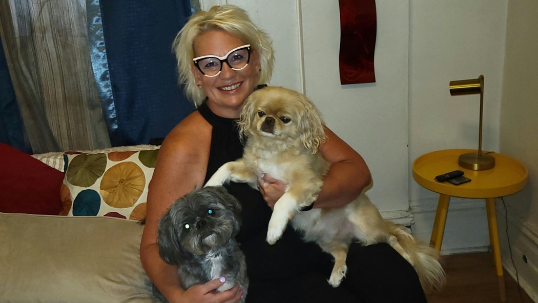 超赞房东坐在她在纽约出租的独立房间的床上，抱着两只小狗。