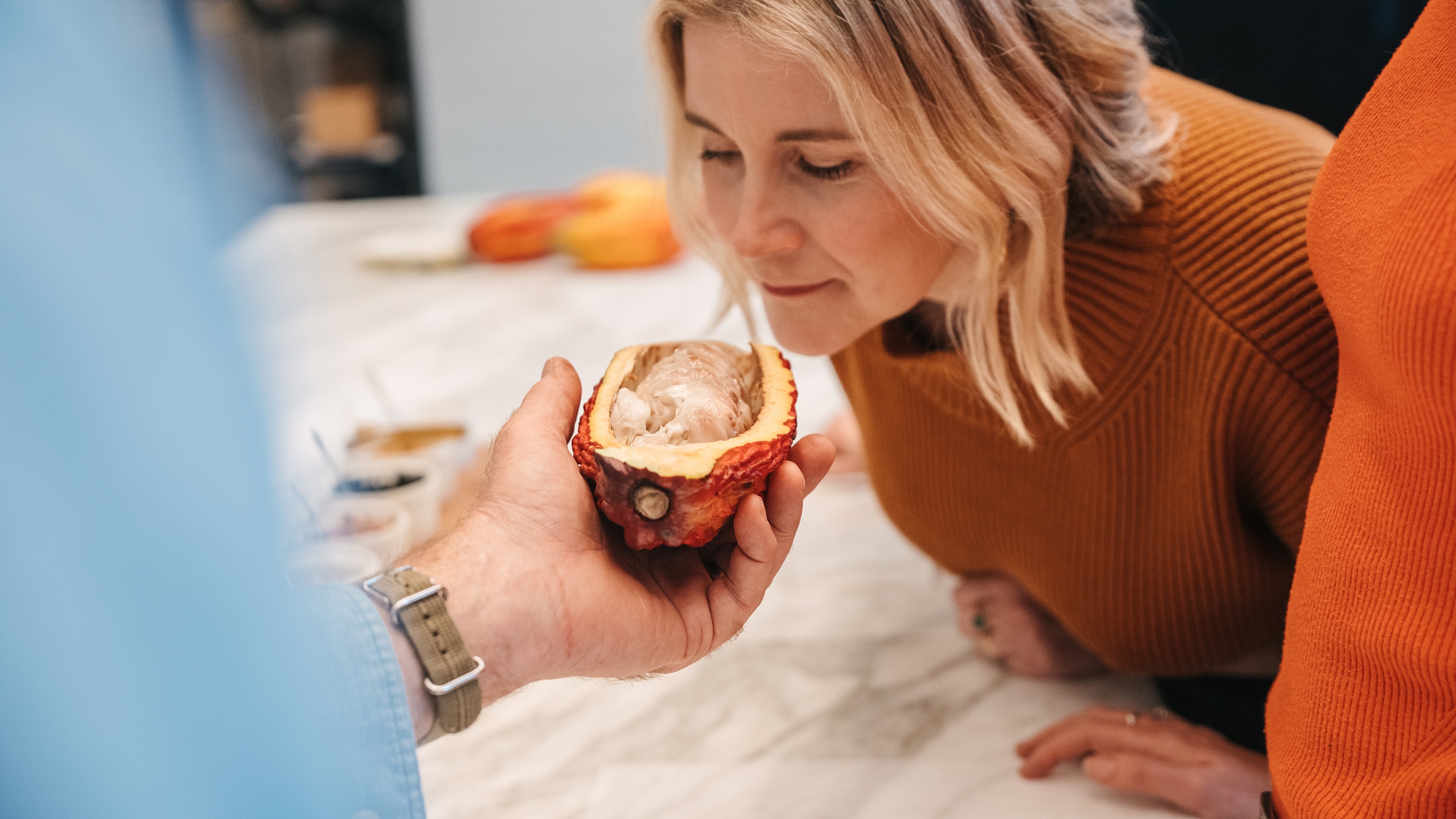 คนสวมเสื้อสเวตเตอร์สีส้มที่มีรอยไหม้โน้มตัวไปเหนือไอแลนด์เตรียมอาหารในครัวเพื่อดมกลิ่นผลไม้ที่หั่นครึ่งไว้