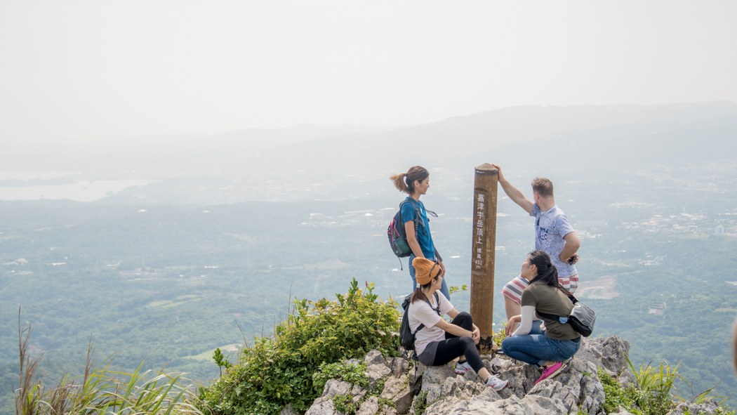 Um anfitrião com seus hóspedes no topo de uma montanha, olhando para uma bela vista