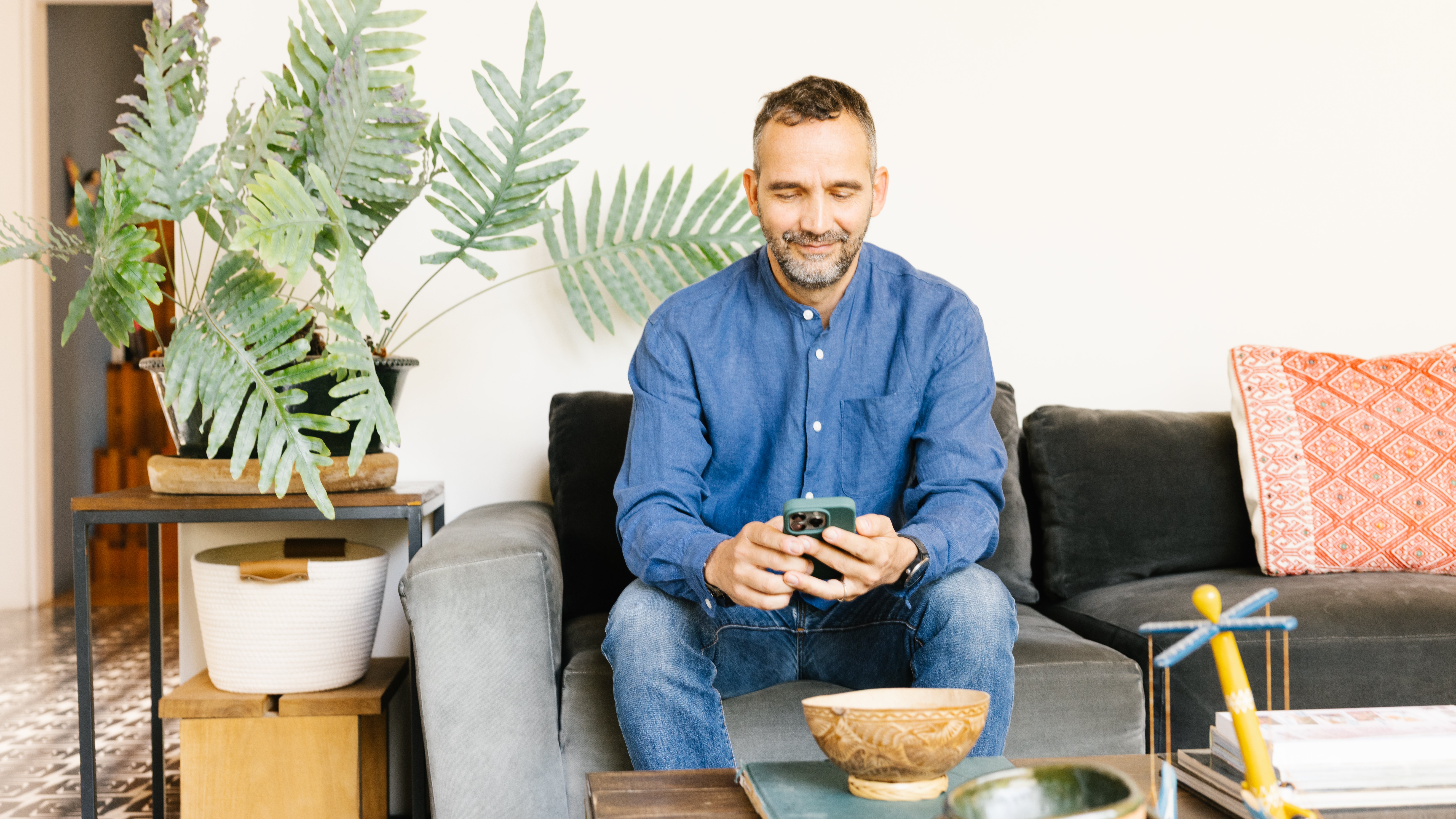 Man sitting on a couch smiling and looking down at an iPhone he holds in his hands.
