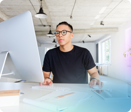 Product manager in glasses working alone at his monitor, writing requirements specific enough for an AI to build from