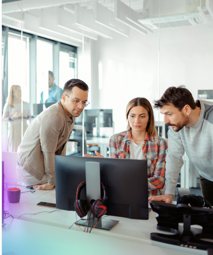 Five colleagues gathered around desktop monitors in an open office, reviewing an AI prototype together