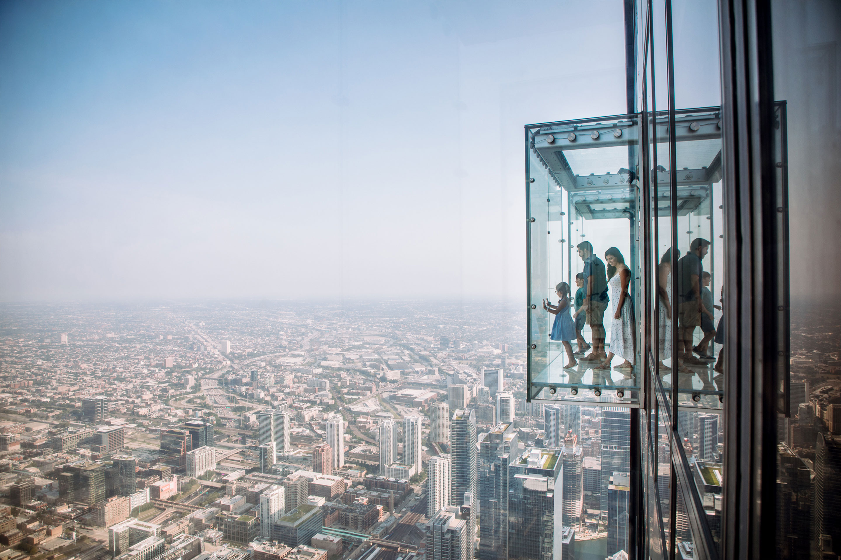 A woman, man, a young boy and young girl stand in a protruding glass box at the Willis Tower SkyDeck.