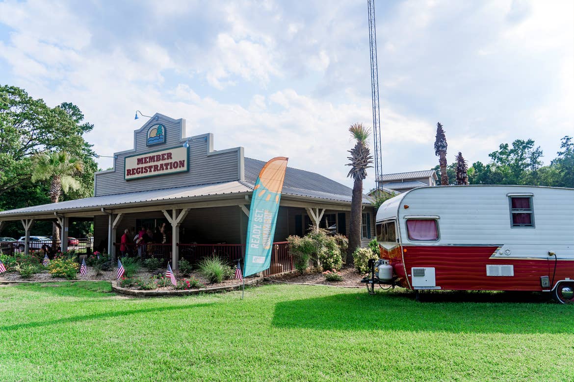 A wooden-sided building with a marquee that reads, 'Member Registration' stands under a cloudy blue sky near a white and red travel camper trailer at the Villages Resort.
