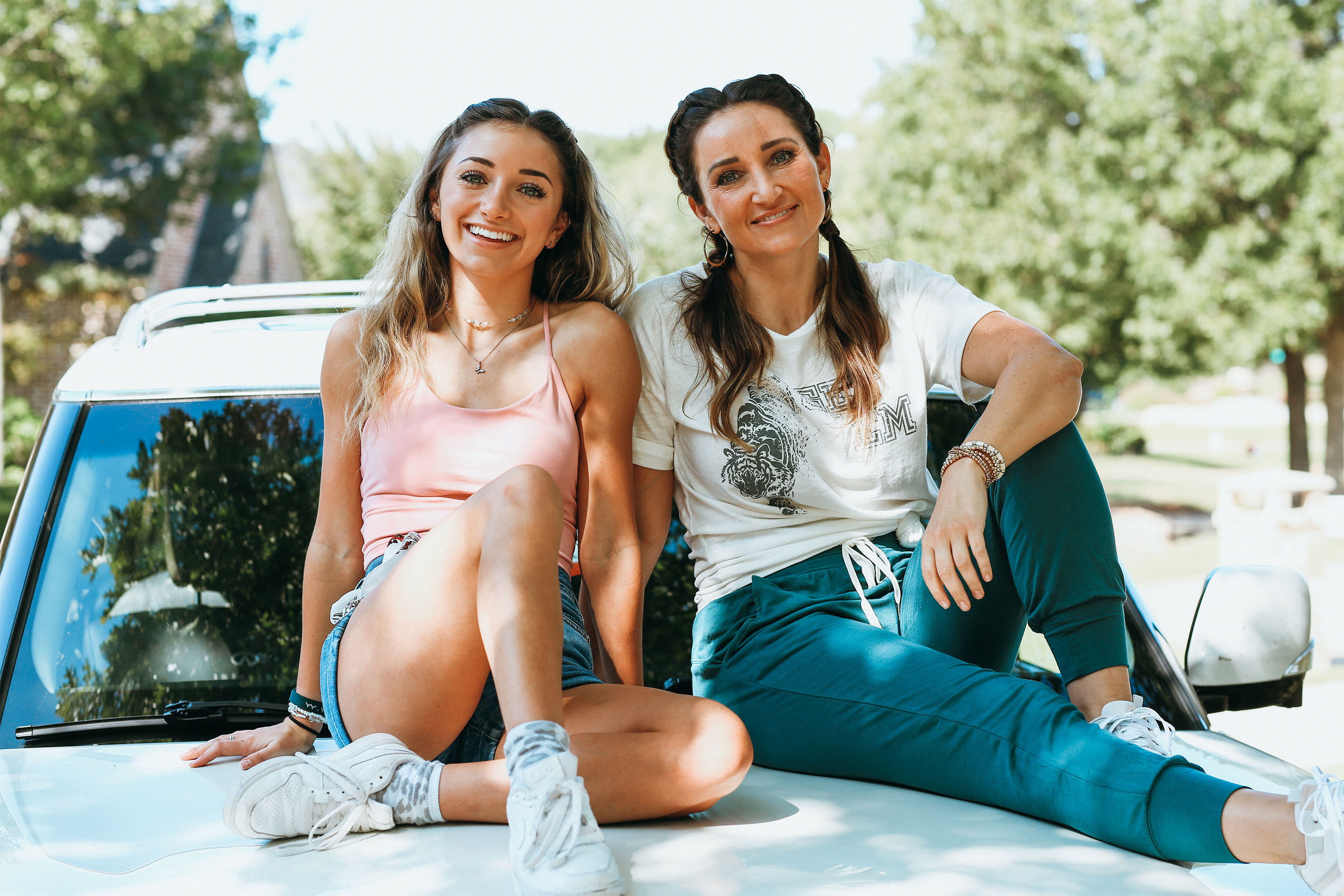 Mindy McKnight (right) and daughter (left) sit outdoors on the hood of a white SUV.