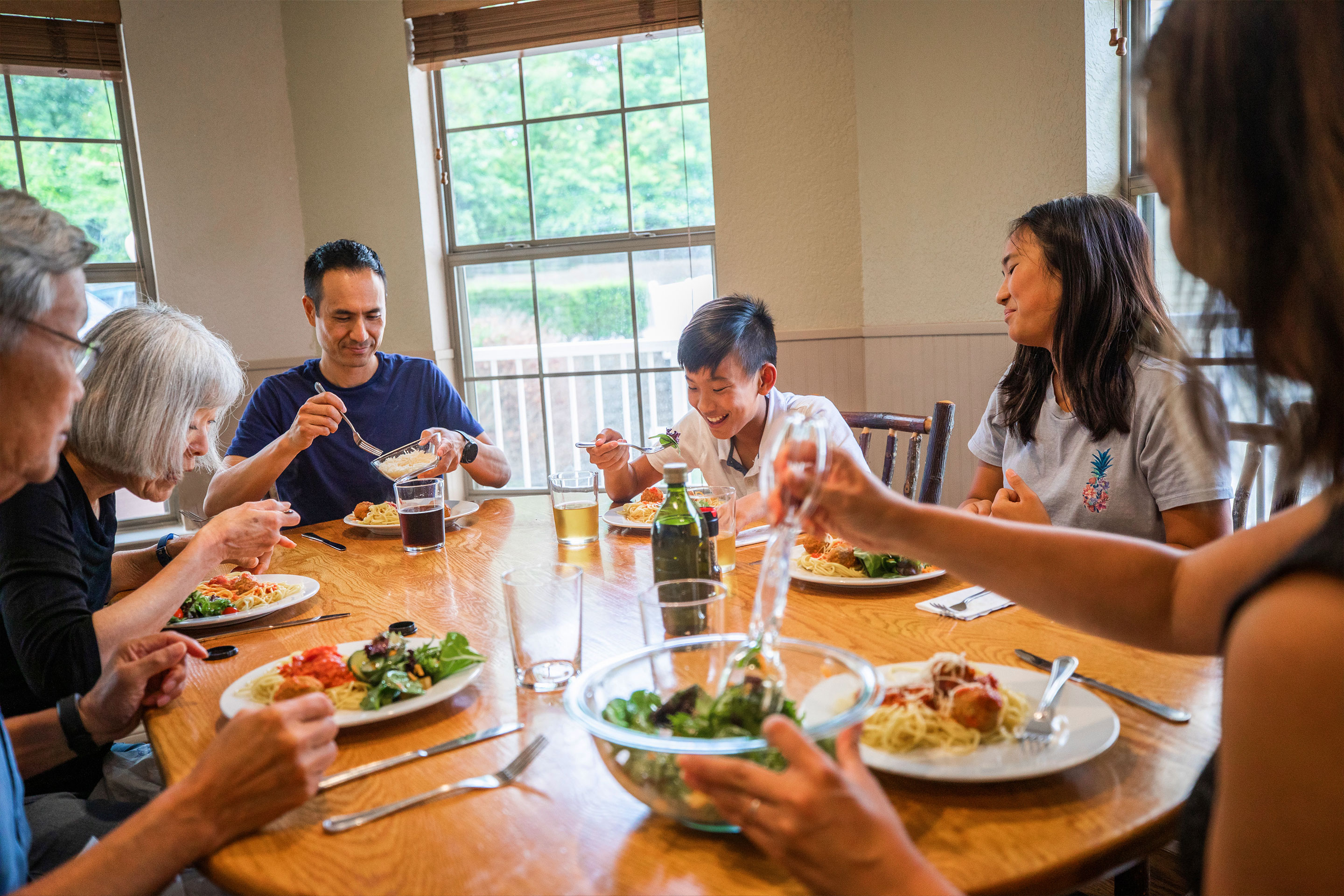 A multigenerational family enjoys dinner at an oblong dining table indoors.