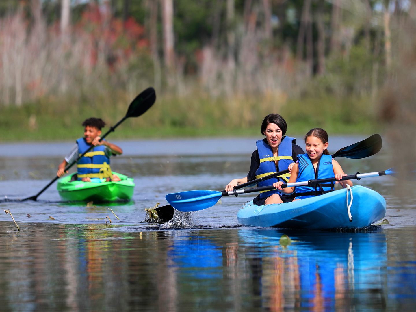Featured Contributor, Clarissa Laskey (middle), kayaks with her daughter (right) in a blue kayak while her son (left) kayaks in his own green kayak.